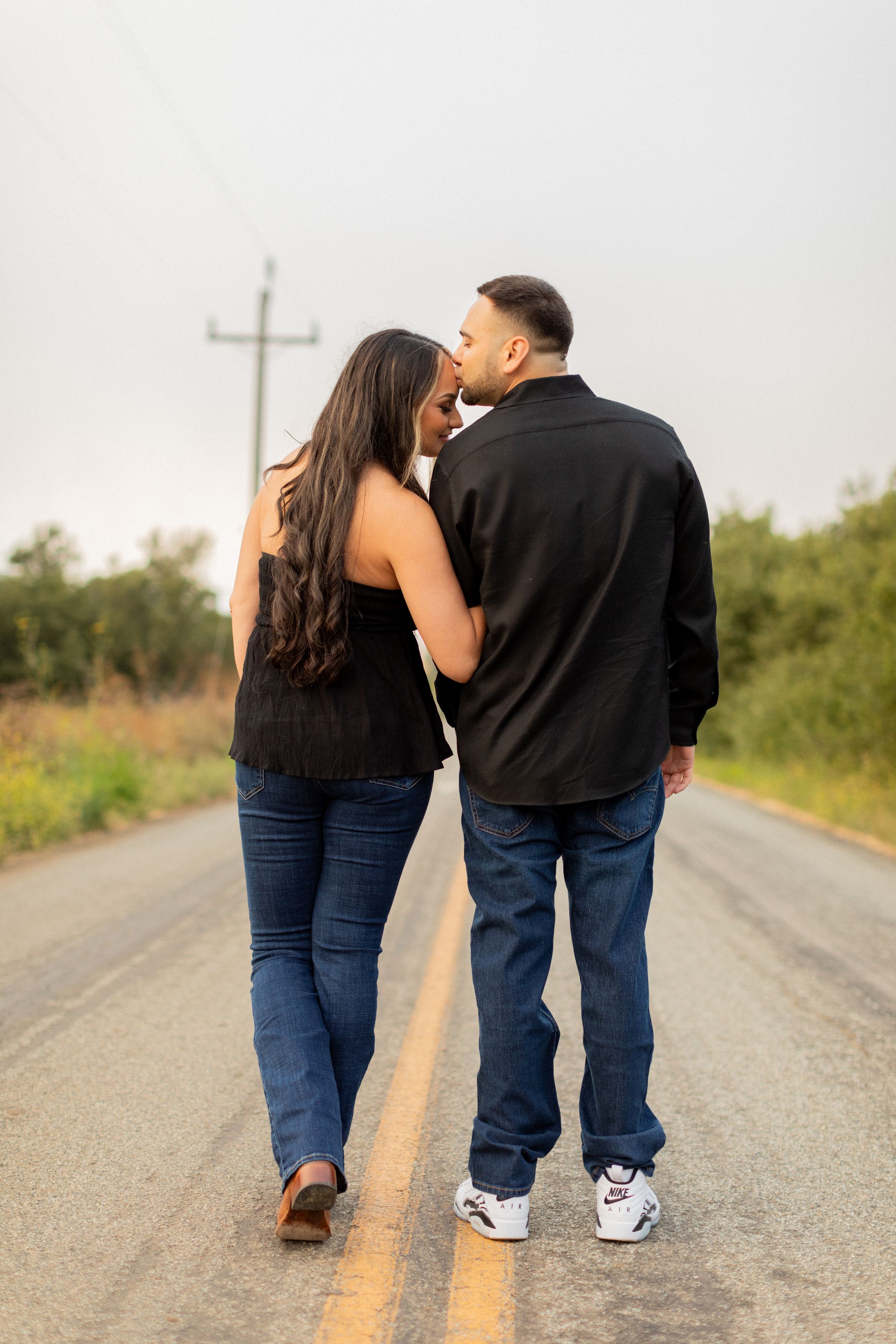 Couple walking together on empty rural road wearing casual denim outfits.