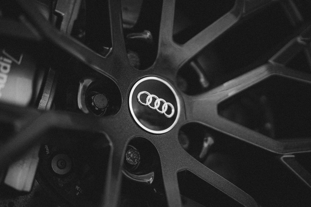 Close-up black and white shot of an Audi wheel center cap with distinctive alloy wheel spokes in the background.