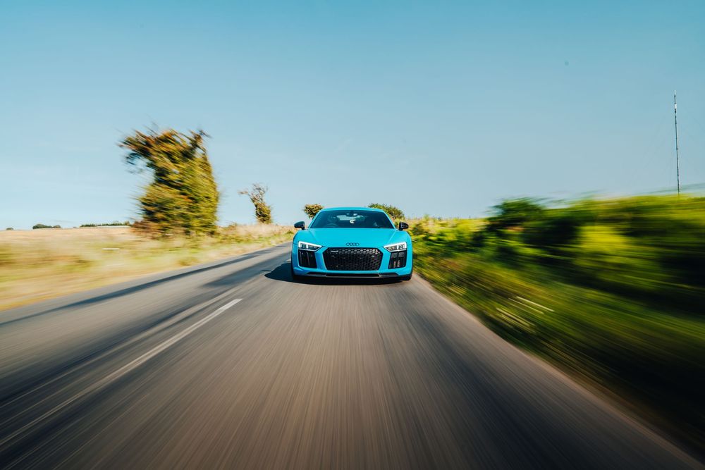 Blue sports car driving on a winding coastal road with ocean and mountains in the background.