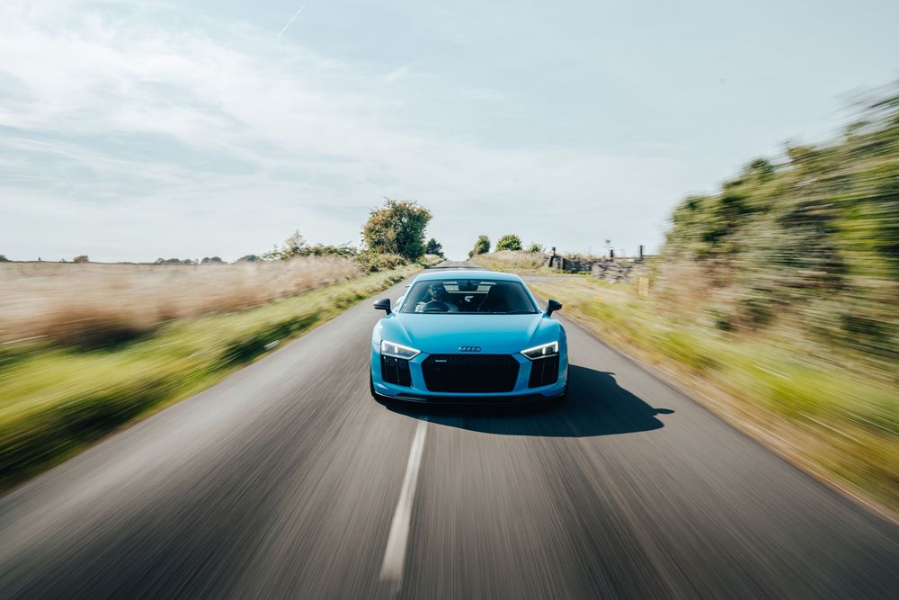 A bright blue Bugatti Chiron supercar speeds along a winding mountain road against a scenic landscape backdrop.
