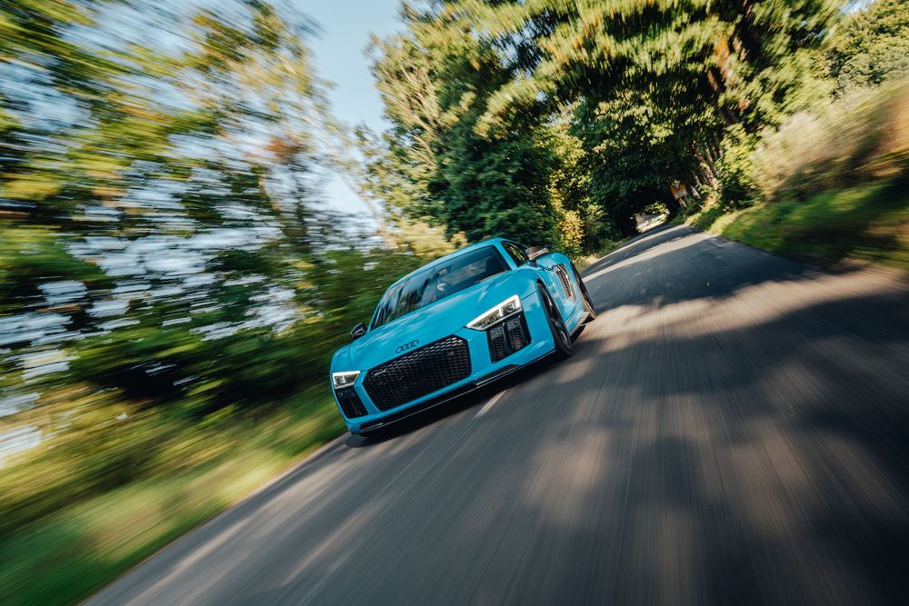 Bright turquoise Porsche sports car driving on a winding mountain road with motion blur effect.