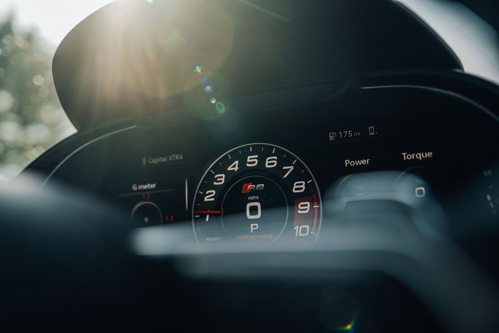 Car dashboard display showing digital speedometer and gauges in dark lighting conditions with lens flare effect.