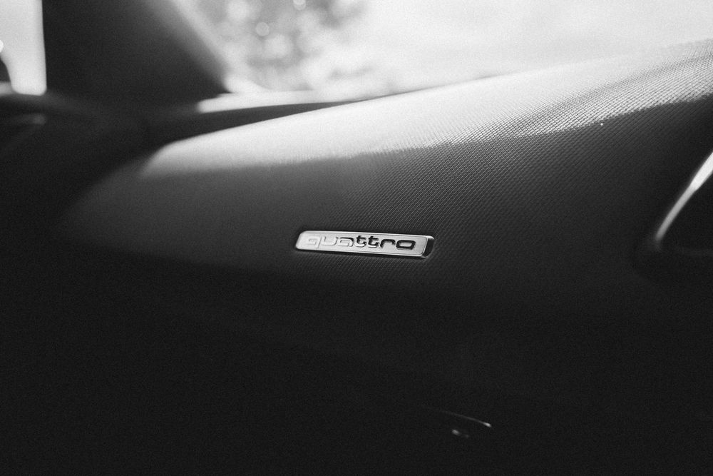 Black and white close-up photo of a car dashboard showing a speedometer and instrument cluster illuminated at night.