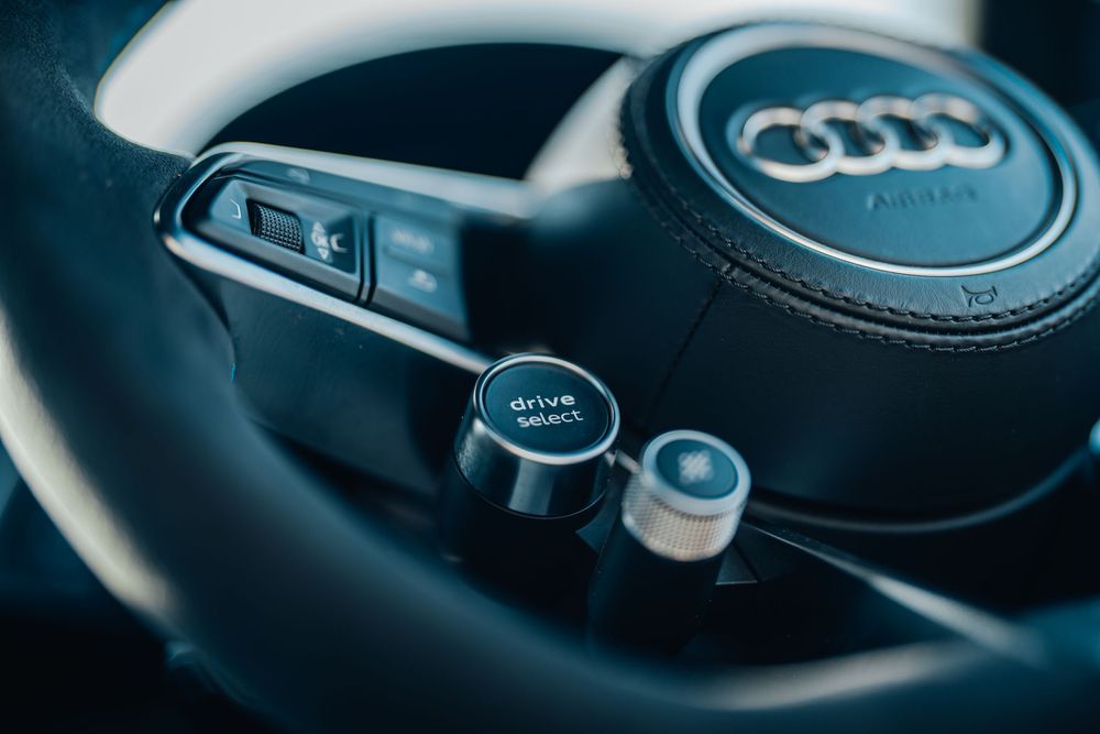 Close-up view of an Audi steering wheel showing the distinctive four-ring logo and controls.