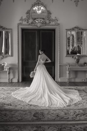 Dramatic black and white photos of a wedding dress with long train in an ornate room with mirrors.