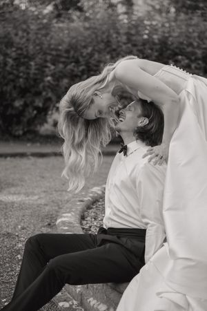 A romantic black and white wedding photo showing a couple sharing an intimate moment outdoors in a garden setting.