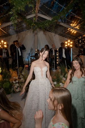 A wedding reception under a tent with string lights and greenery as guests dance while a band performs on stage.