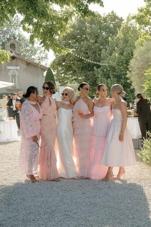 A group wearing matching pink dresses poses together at an outdoor wedding venue.