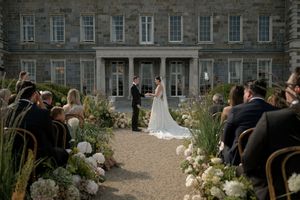 Outdoor wedding ceremony setup with white floral arrangements in front of a historic stone building.