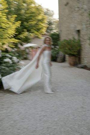 Motion blur of white dresses twirling on a stone patio with green foliage in background.