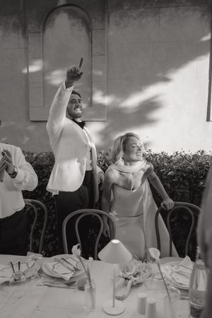 Black and white sequence showing a person in white clothing making dramatic gestures at a dining table.