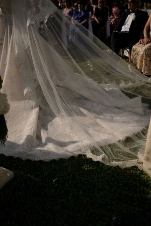 Bride's elegant lace wedding dress train and veil spread across the aisle during outdoor ceremony.