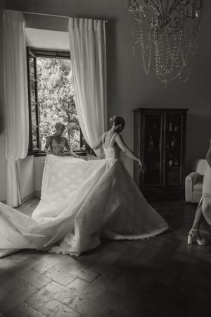Black and white photo of a bride in an elegant lace gown with a long train in a classic Italian villa room.
