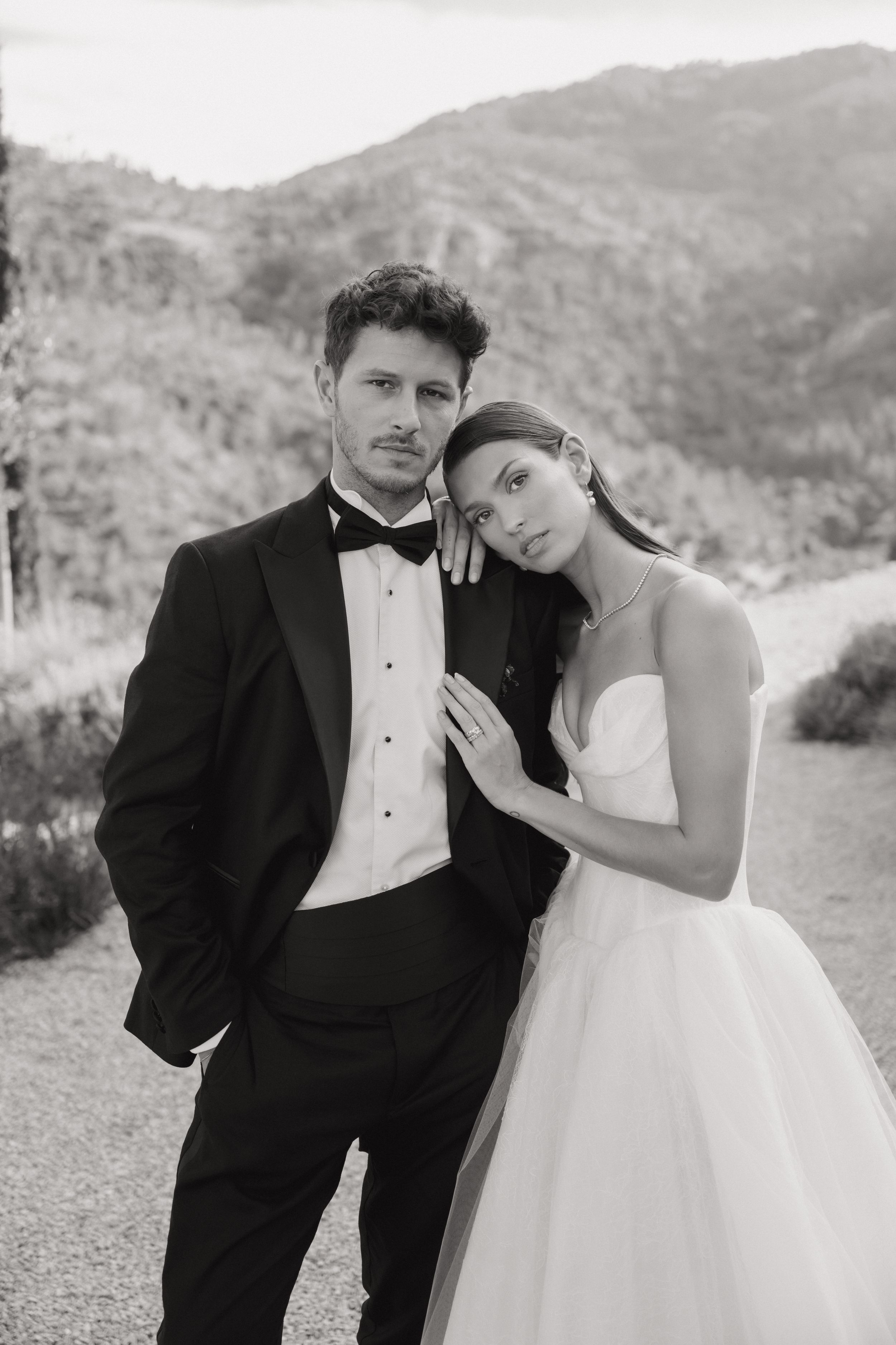 Black and white wedding portraits of a couple embracing outdoors with mountains in the background.