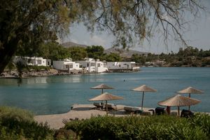 Scenic lakeside view with thatched umbrellas and boats dotting the tranquil waterfront on a sunny day.