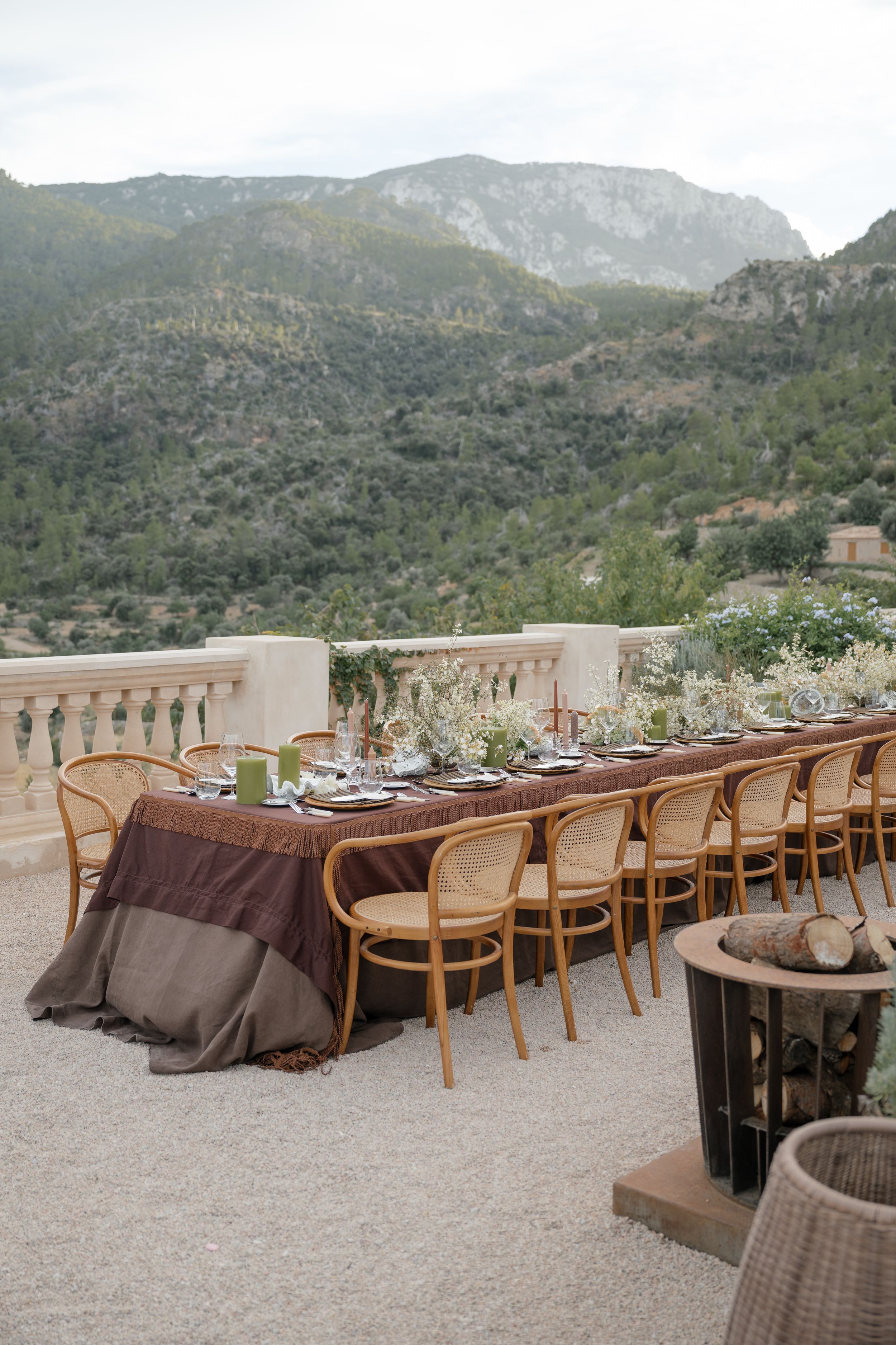 Long rustic dining table setup on terrace overlooking mountain landscape with brown tablecloths.