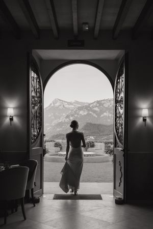 A silhouetted figure stands in an ornate doorway overlooking a majestic mountain landscape in black and white.