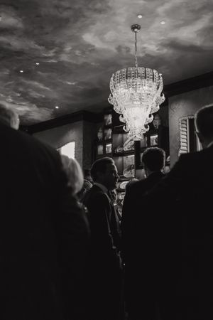 Elegant crystal chandeliers illuminate a dark room filled with silhouettes of people at a formal gathering.