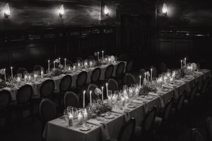 Long banquet tables with elegant place settings and glowing candlelight create an intimate dining atmosphere.
