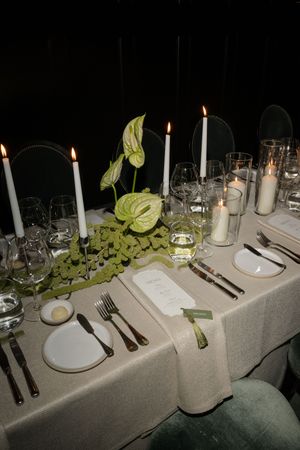 An elegant wedding table setting with white candles, greenery, and place settings on a gray tablecloth.