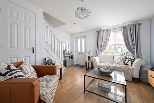 Modern living room interior with brown leather sofa, gray curtains, hardwood floors and white walls in natural light.