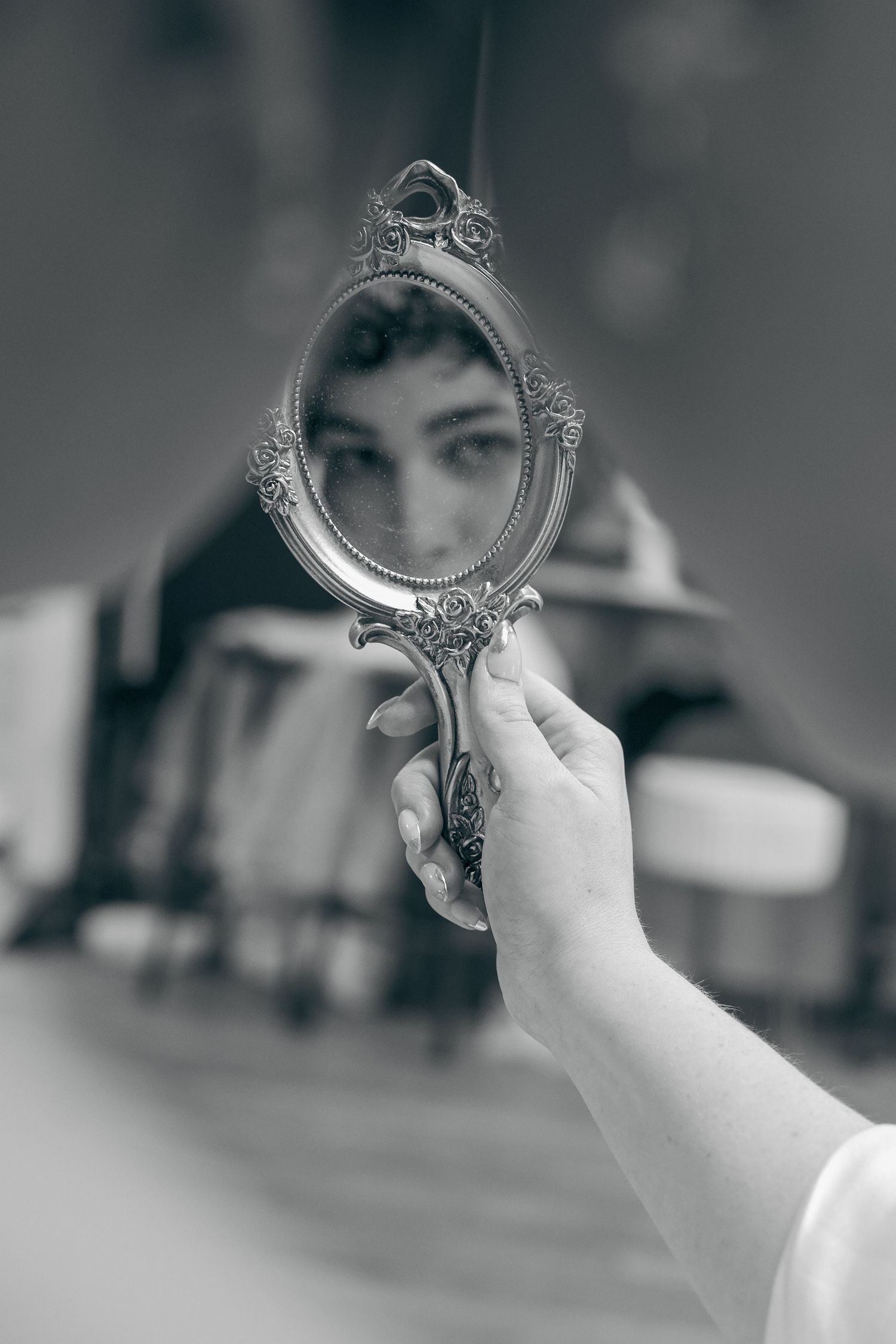 A hand holds up an ornate silver handheld mirror against a blurred background.