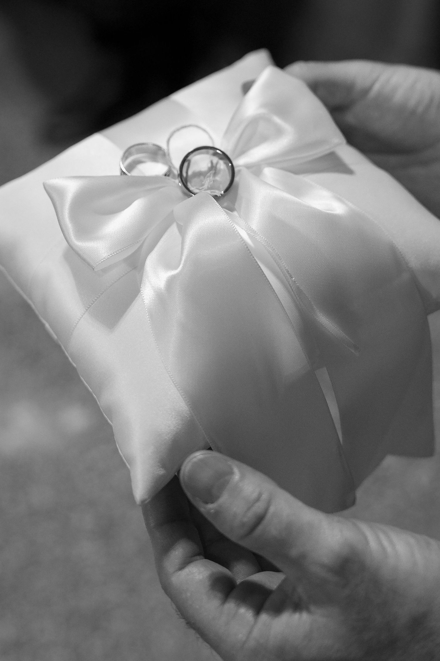 A close-up series showing hands gently placing a white satin ring pillow with delicate ribbons and bows.