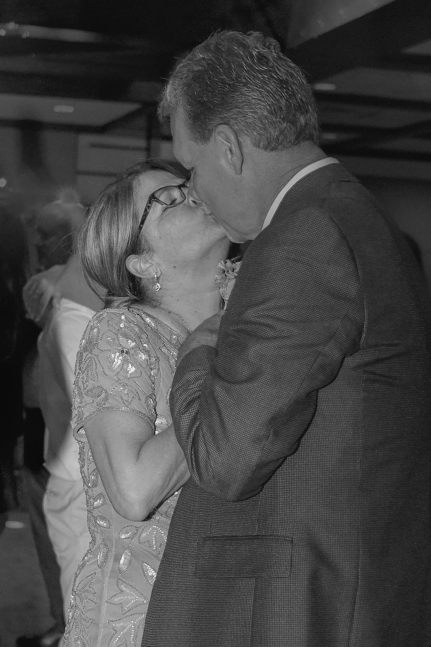 A couple embraces and kisses on a dance floor in a black and white vintage photograph.