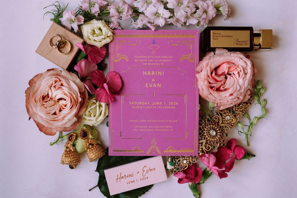 Pink and gold wedding invitations styled with blush roses and floral arrangements on a light background.