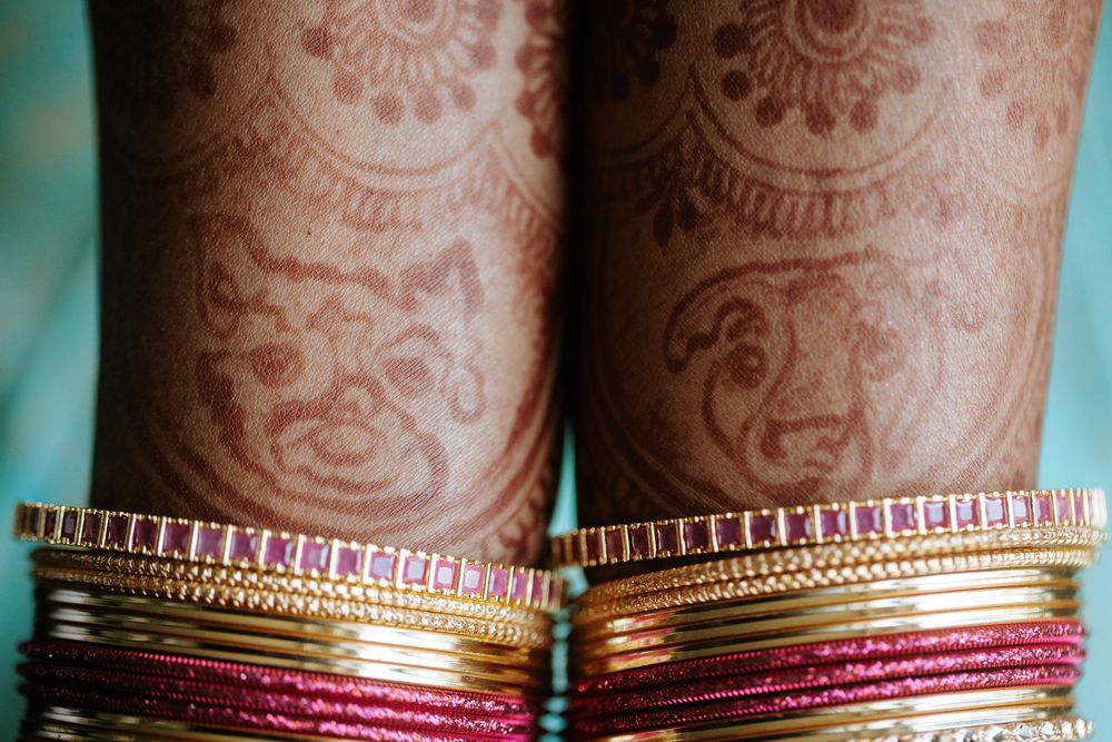 Close-up view of colorful pink and gold bangles stacked on brown henna decorated arms.