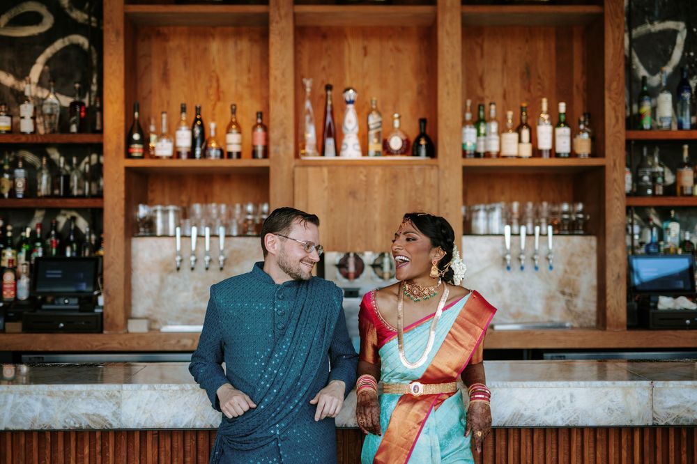 A couple enjoying drinks and conversation at a cozy wooden bar with bottles displayed on shelves behind them.