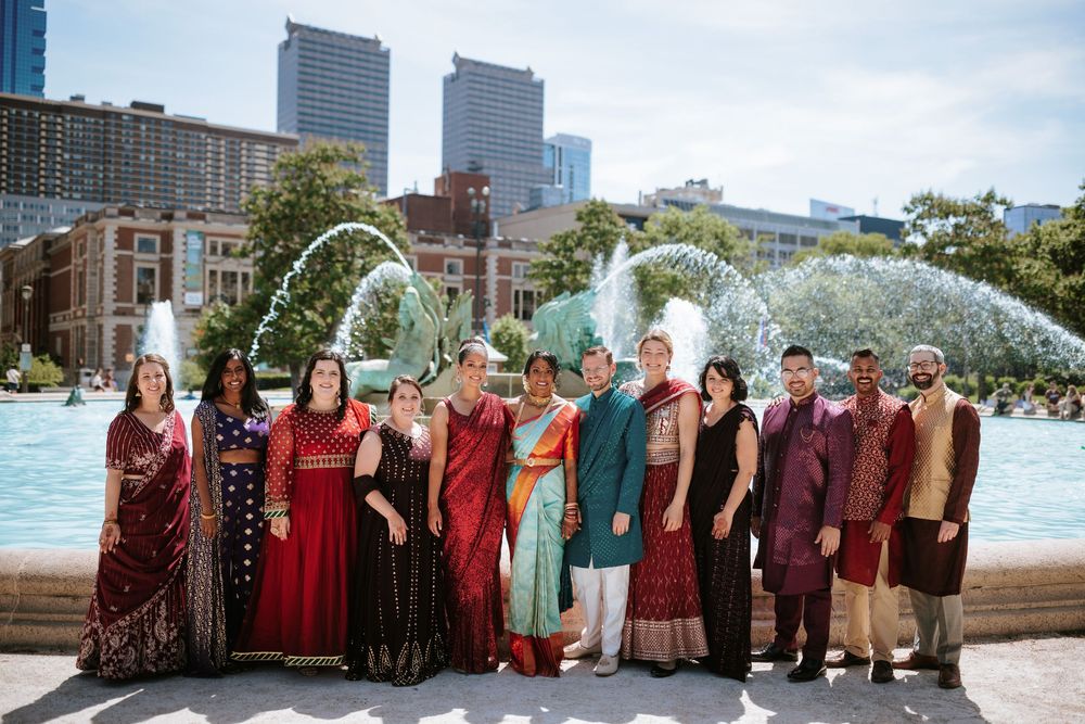 Wedding party members in burgundy and neutral tones pose in front of an urban cityscape.
