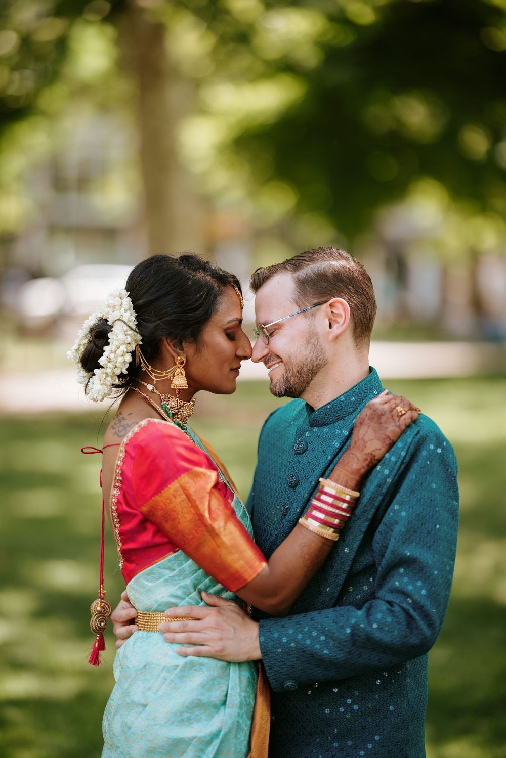 A romantic couple in traditional Indian and Western attire share intimate moments in a sunlit park setting.