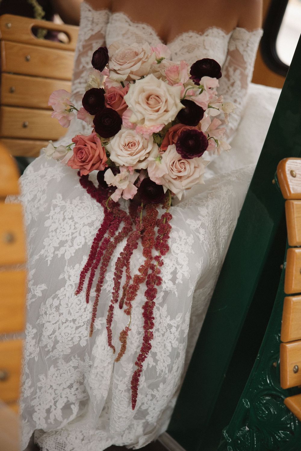 Close-up details of a white lace wedding dress adorned with burgundy and blush pink floral arrangements.