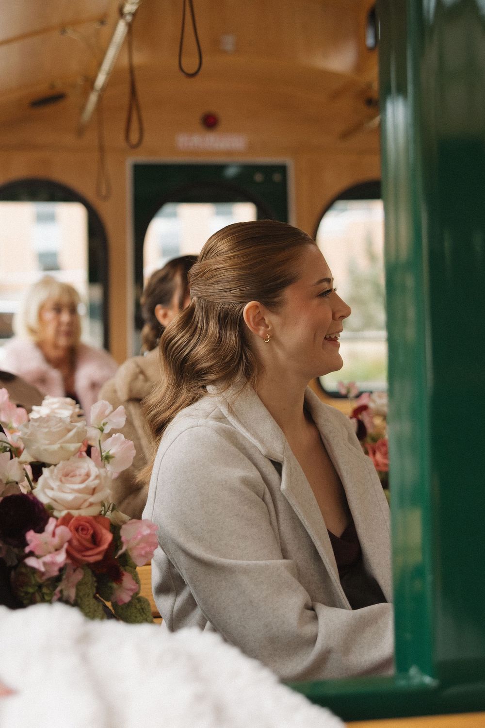 A person in a light coat laughs joyfully while sitting in a vintage train car with pink roses visible.