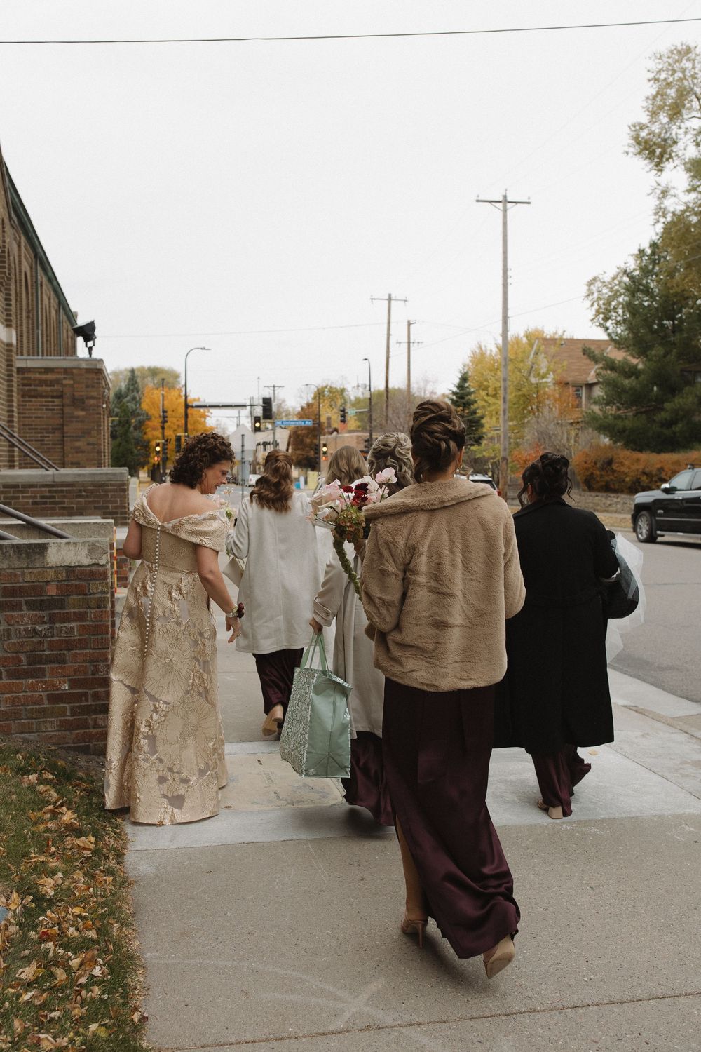 A group walking down a sidewalk in vintage-style period clothing on an autumn day.