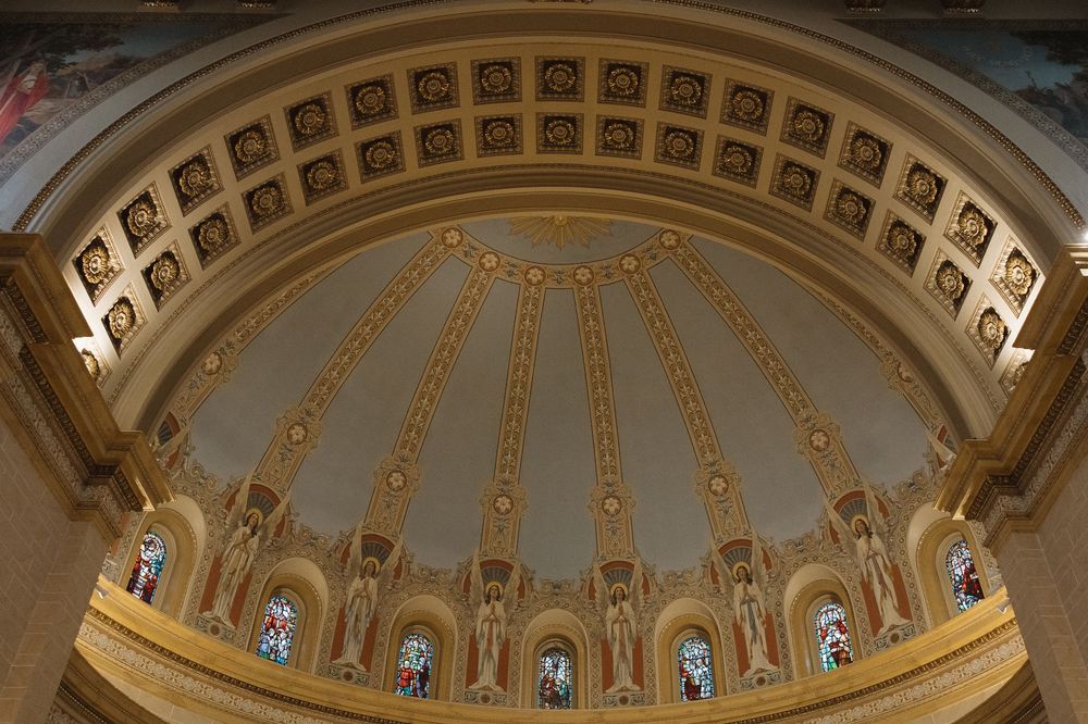 Ornate cathedral ceiling with golden dome architecture featuring stained glass windows and detailed religious artwork.