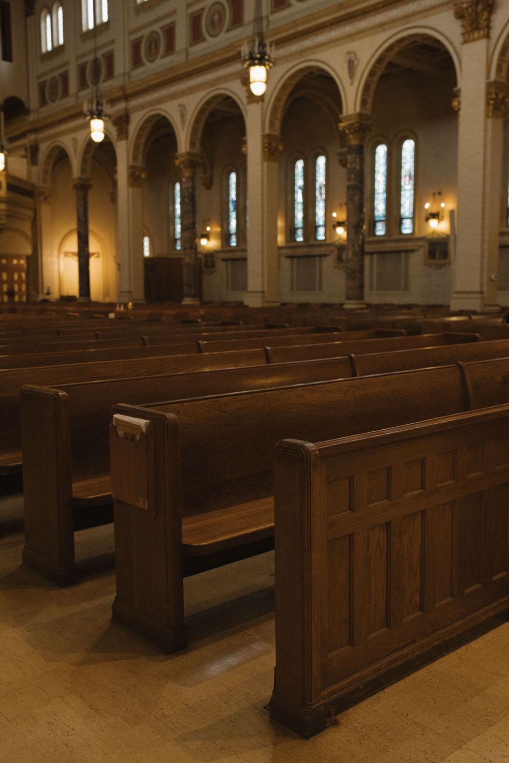 Rows of polished wooden church pews line the interior of a historic cathedral with ornate architectural details and lighting.
