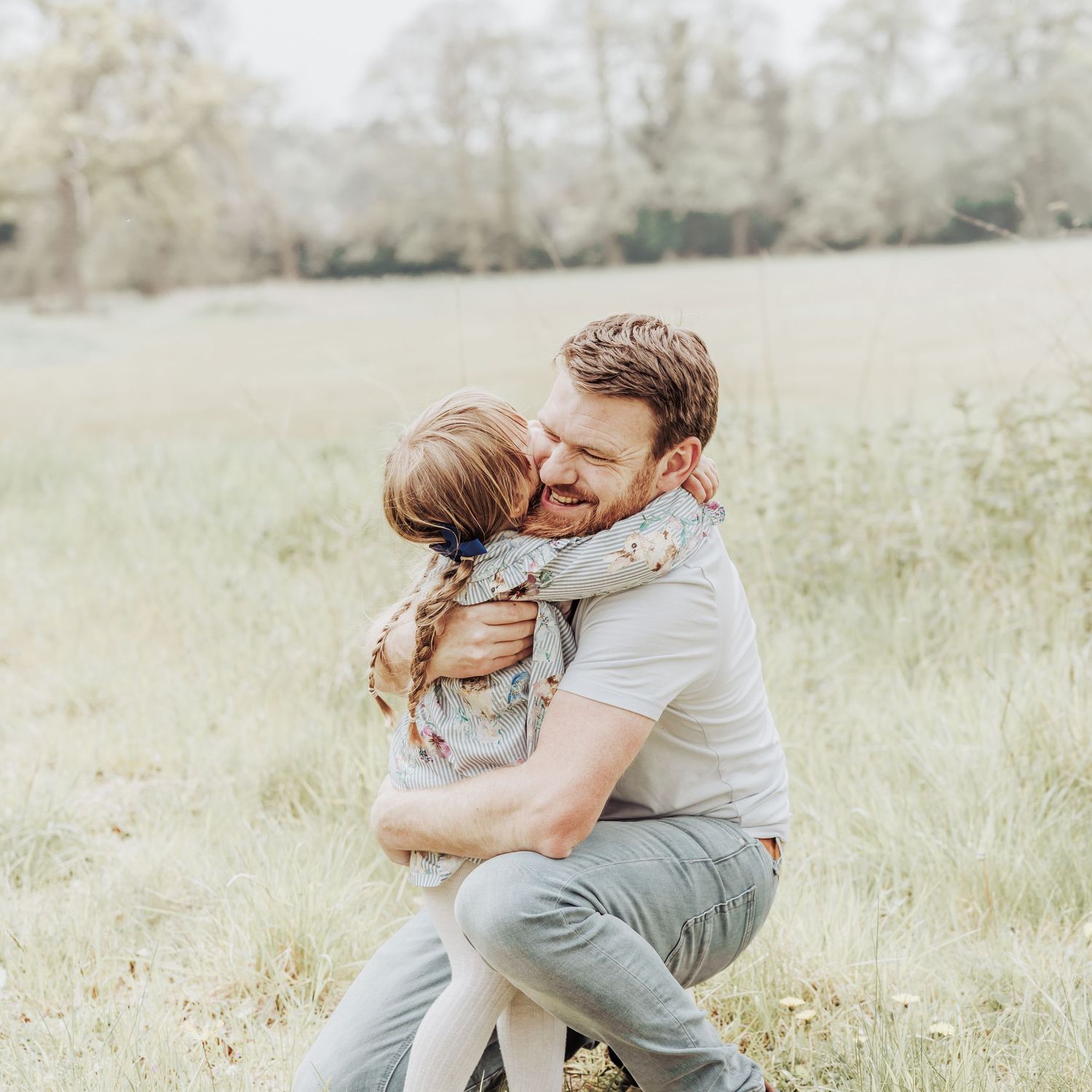 Natural family photography moment of a parent cuddling their child in an open field, showing real emotion and closeness.