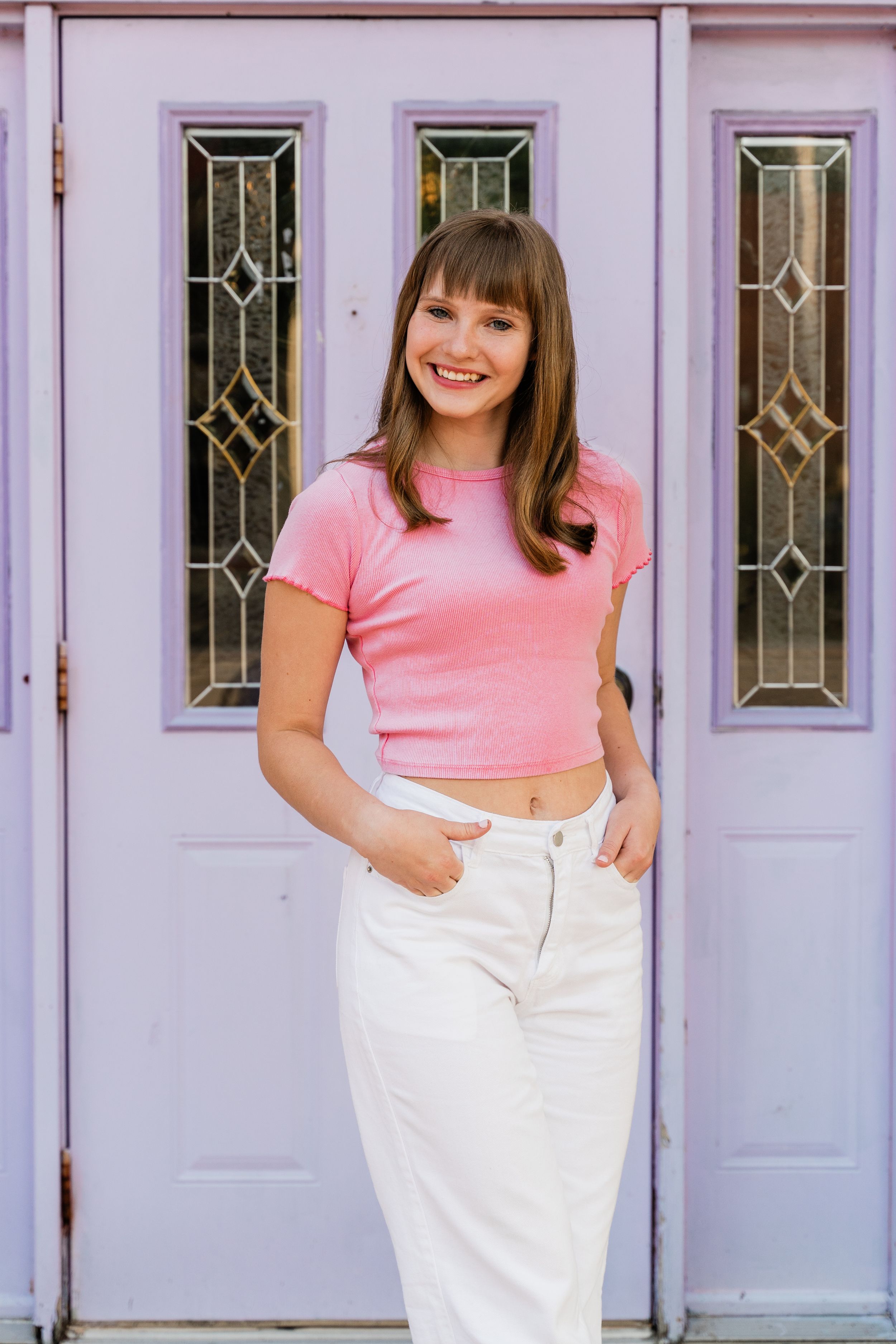 A person in a pink crop top and white jeans stands in front of a lavender door with decorative glass panels.