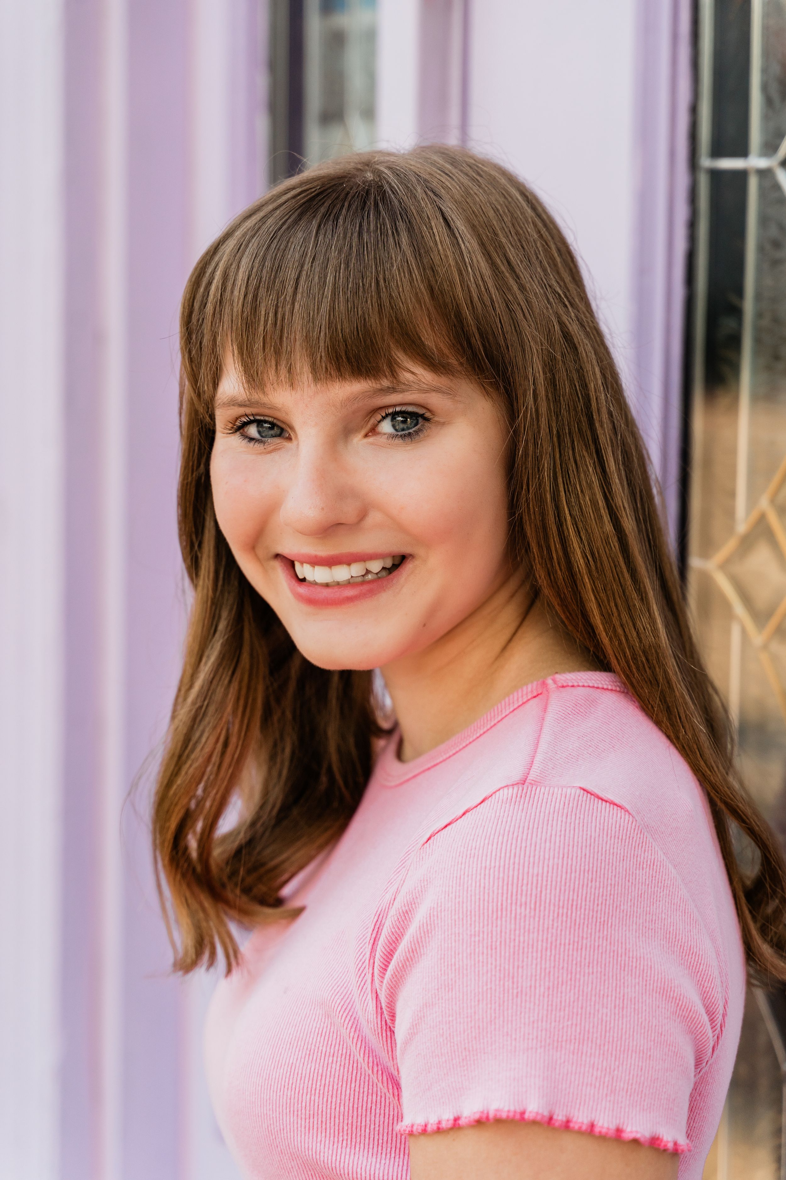 A person in a pink sweater smiles warmly while posing against a light purple background.