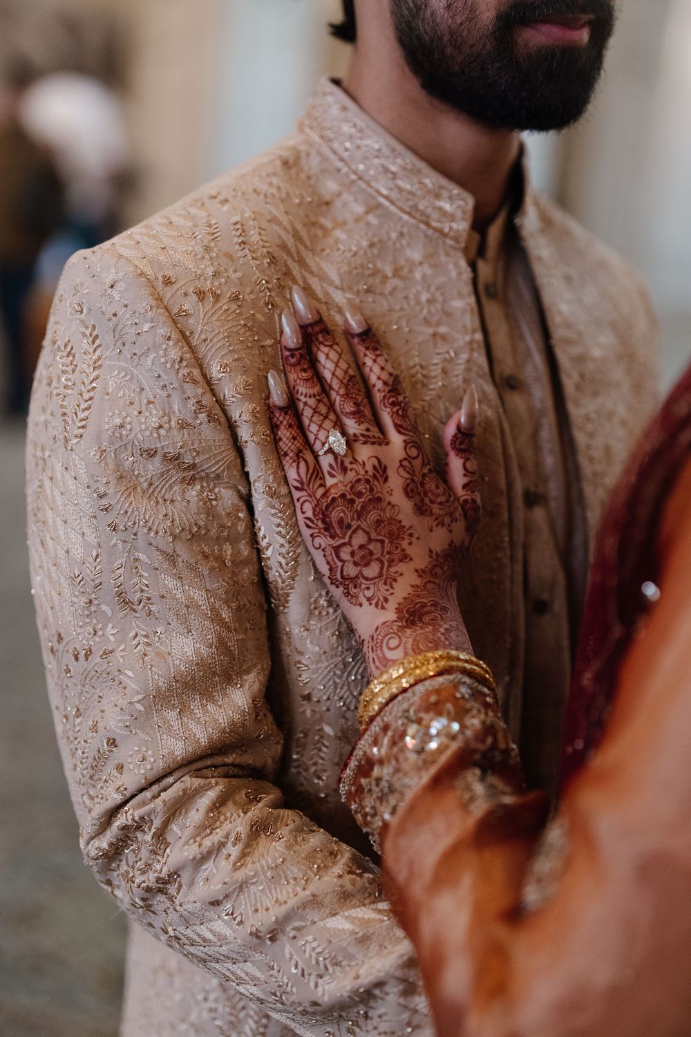Bride with intricate henna mehndi design and gold bangles placing hand on grooms sherwani chest.