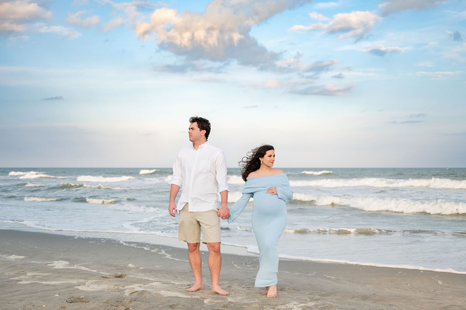 Couple walking along a serene beach with gentle waves and cloudy sky.