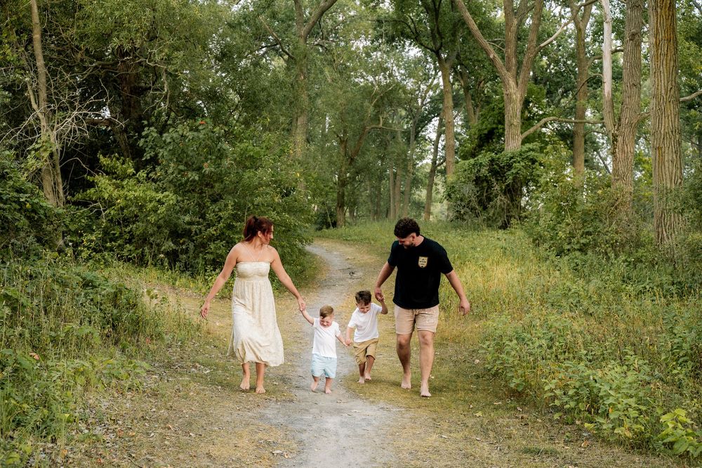 A family walks together along a tree-lined nature path during a sunny summer day.