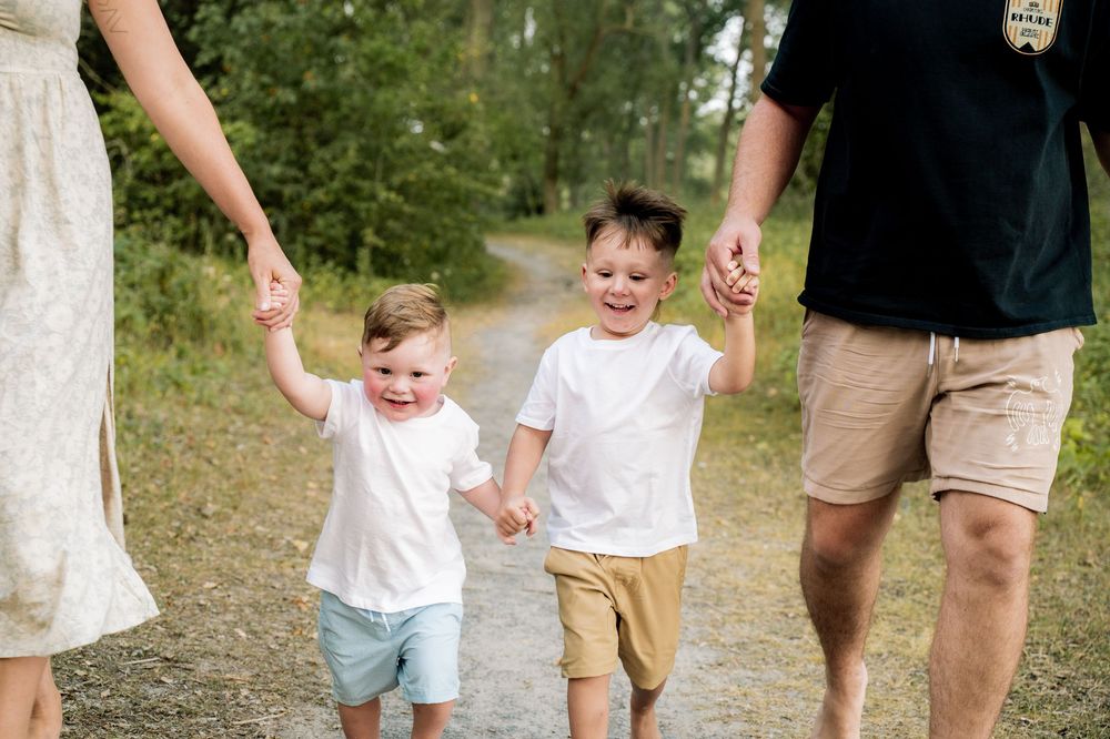Children walking in a line holding hands while exploring a nature trail on a sunny day.