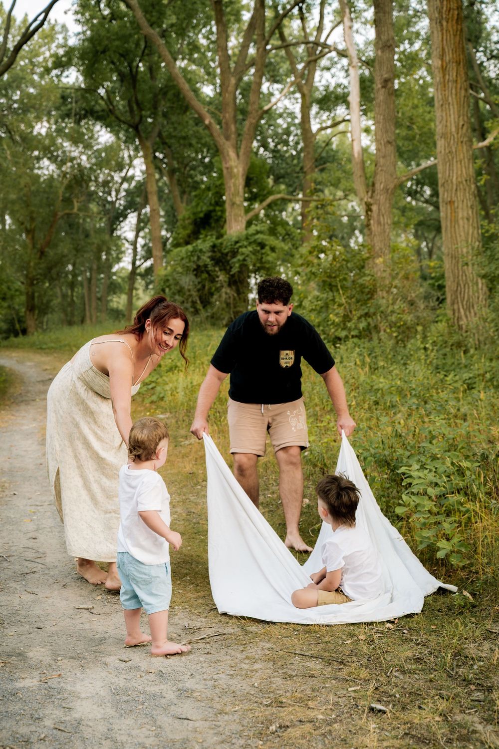 A series of candid photos captures a family playing together with a white blanket along a forest path.