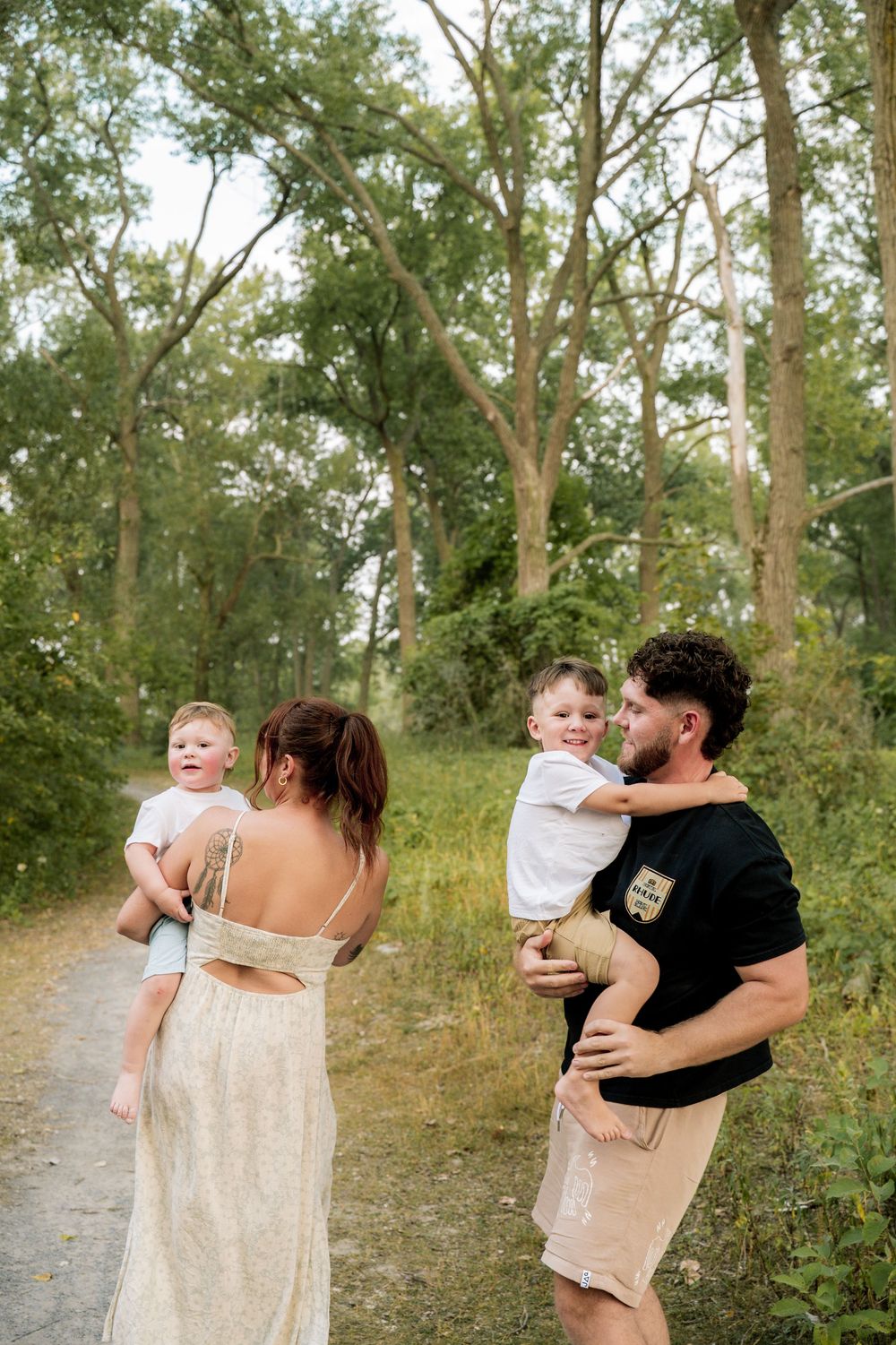 Playful family photos captured on a sandy beach path surrounded by lush green trees and vegetation.