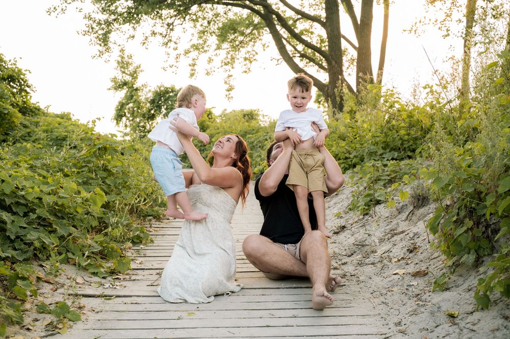 Candid family moments shared on a sandy beach trail with natural greenery in the background.