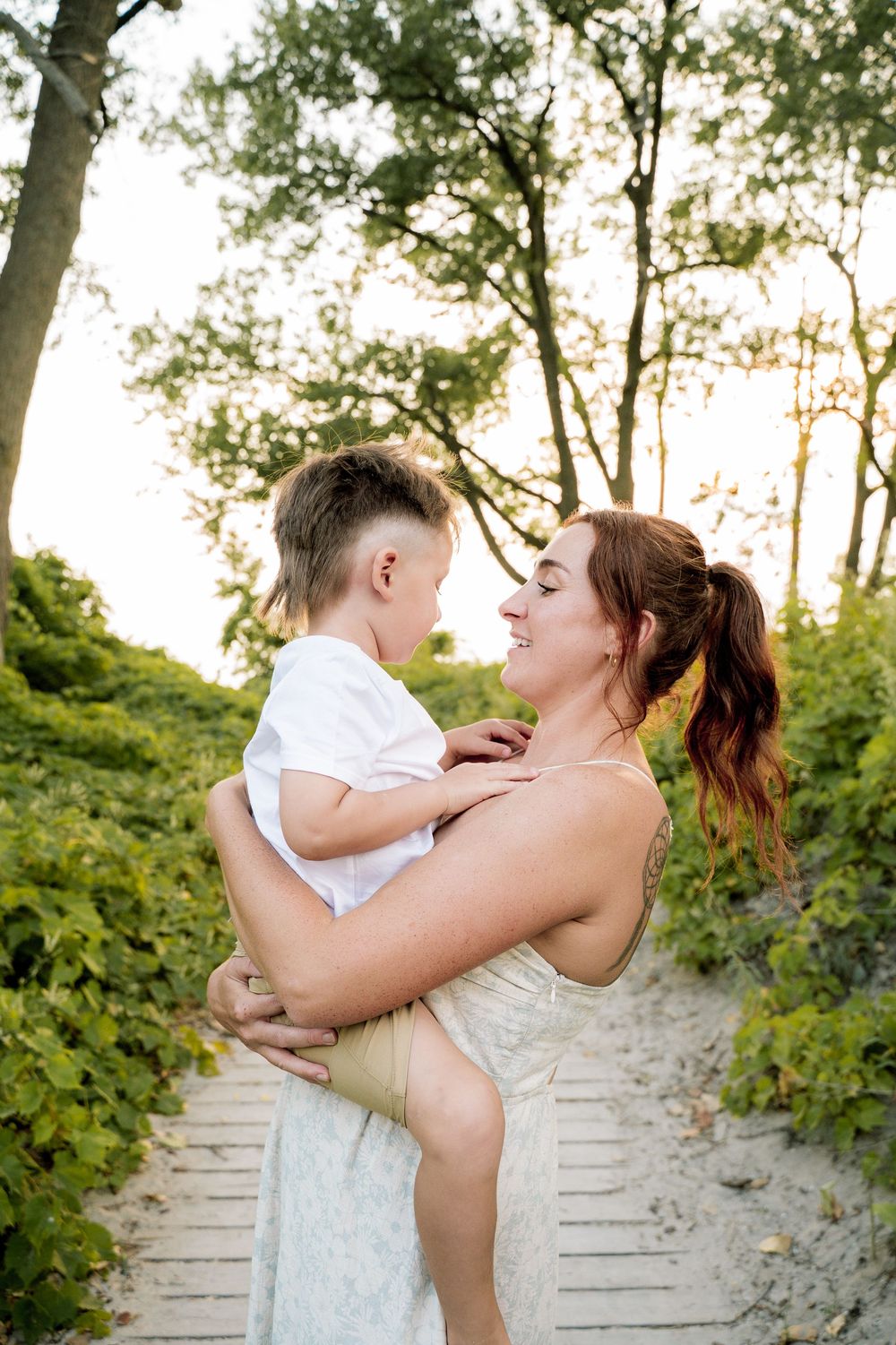 A romantic couple embraces on wooden steps surrounded by trees and greenery.