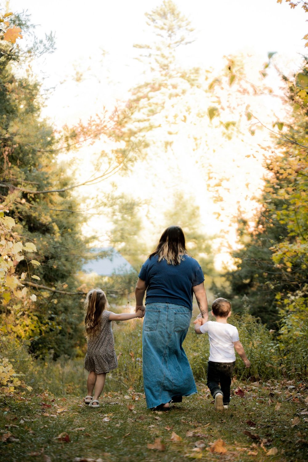 A small group walks down a wooded trail during golden hour with sunlight filtering through trees.